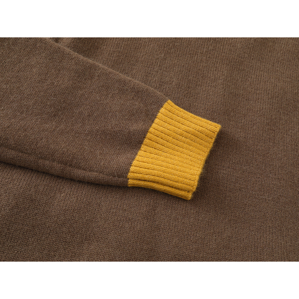 Close-up of a brown knit sweater sleeve ending in a mustard yellow ribbed cuff.