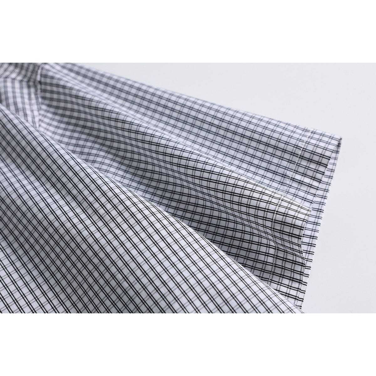 Close-up of the white-and-black plaid shirt sleeve and cuff with visible stitching.