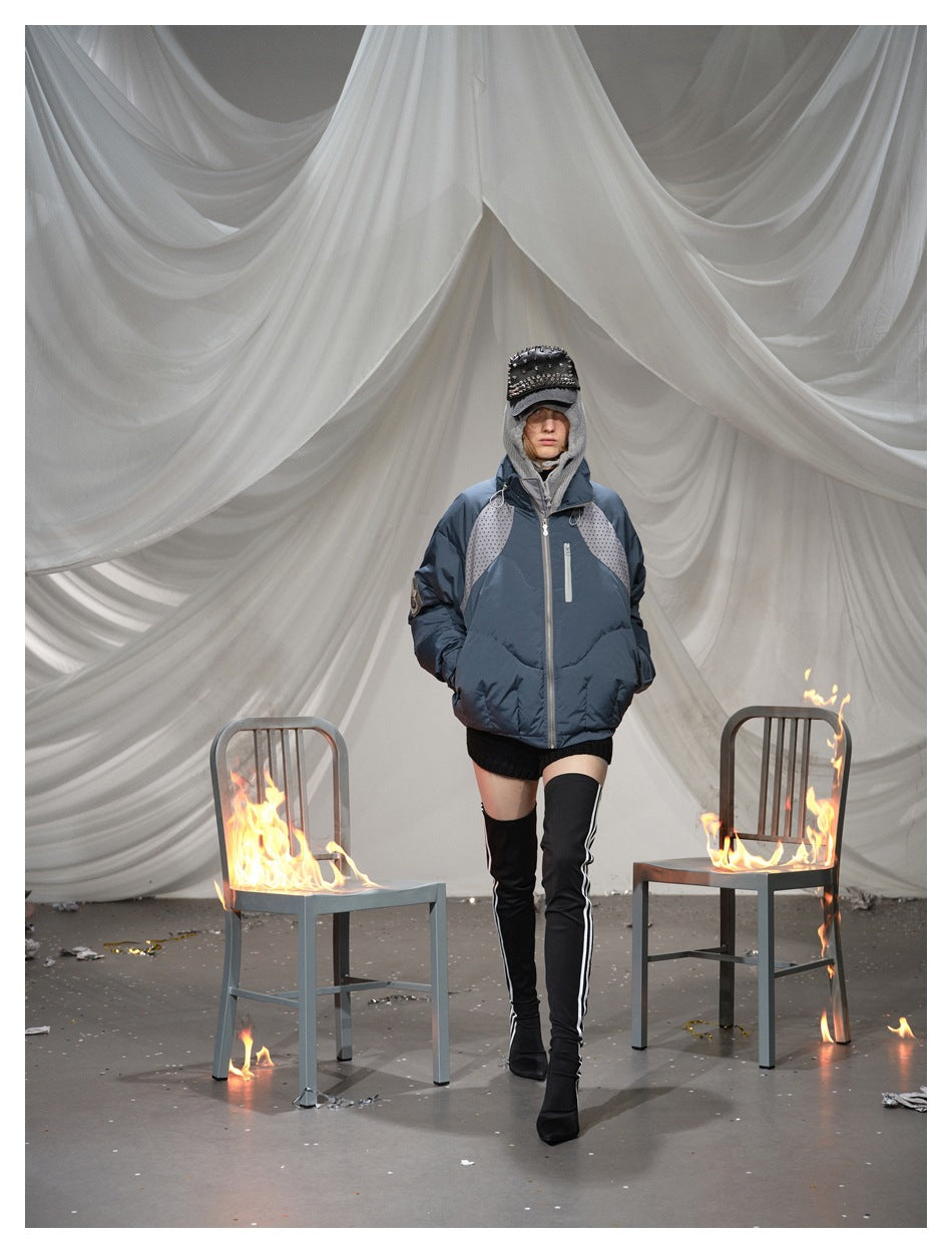 Full-length model wearing a blue-gray padded jacket with dotted shoulder panels in a draped studio set.