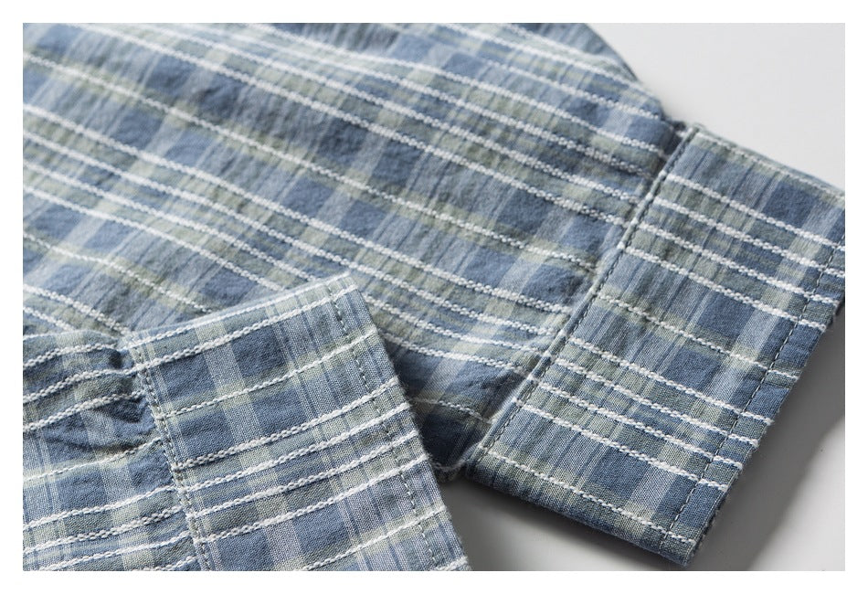 Close-up of blue-gray plaid garment fabric with stitched hems and folded edges.