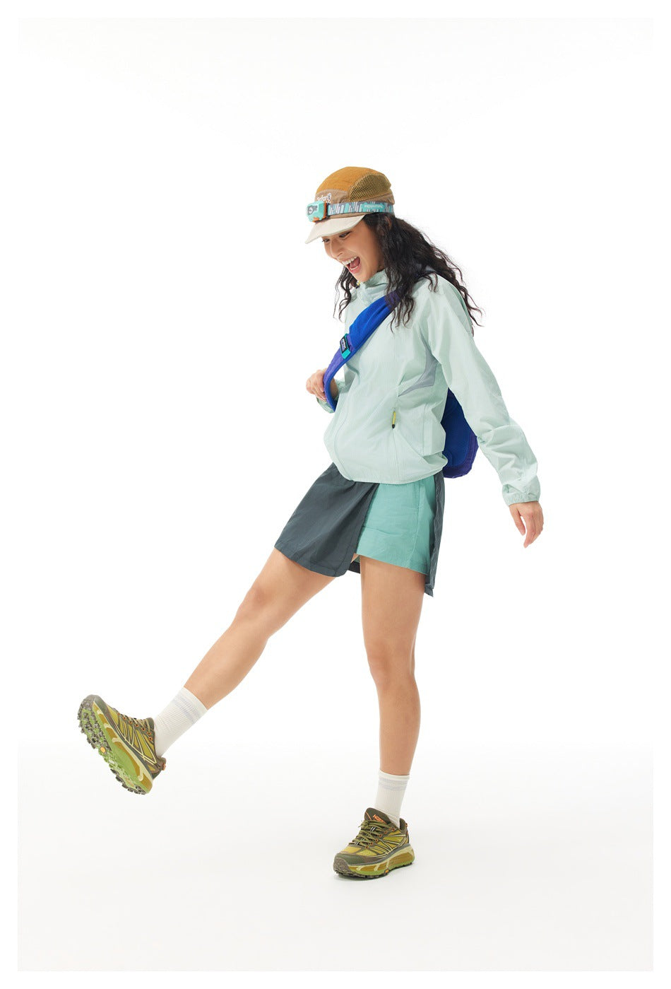 Model in a pale mint hooded jacket and two-tone dark teal skirt, shown in profile with a blue crossbody bag.