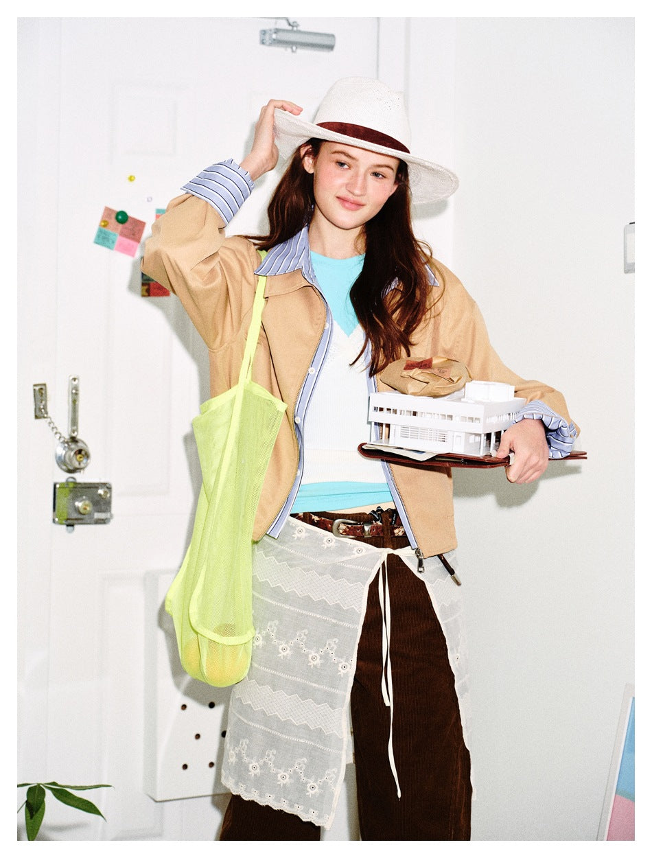 Model wearing a tan zip-front jacket with blue striped collar and cuffs, styled with a white hat and lace apron.