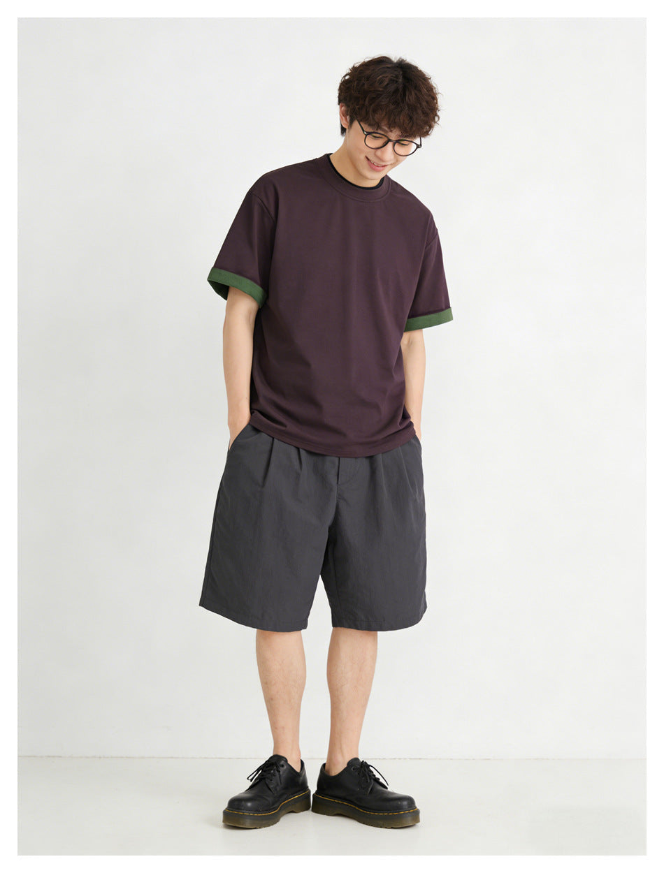 Model wearing a dark plum short-sleeve crew-neck T-shirt with green sleeve-cuff trim.