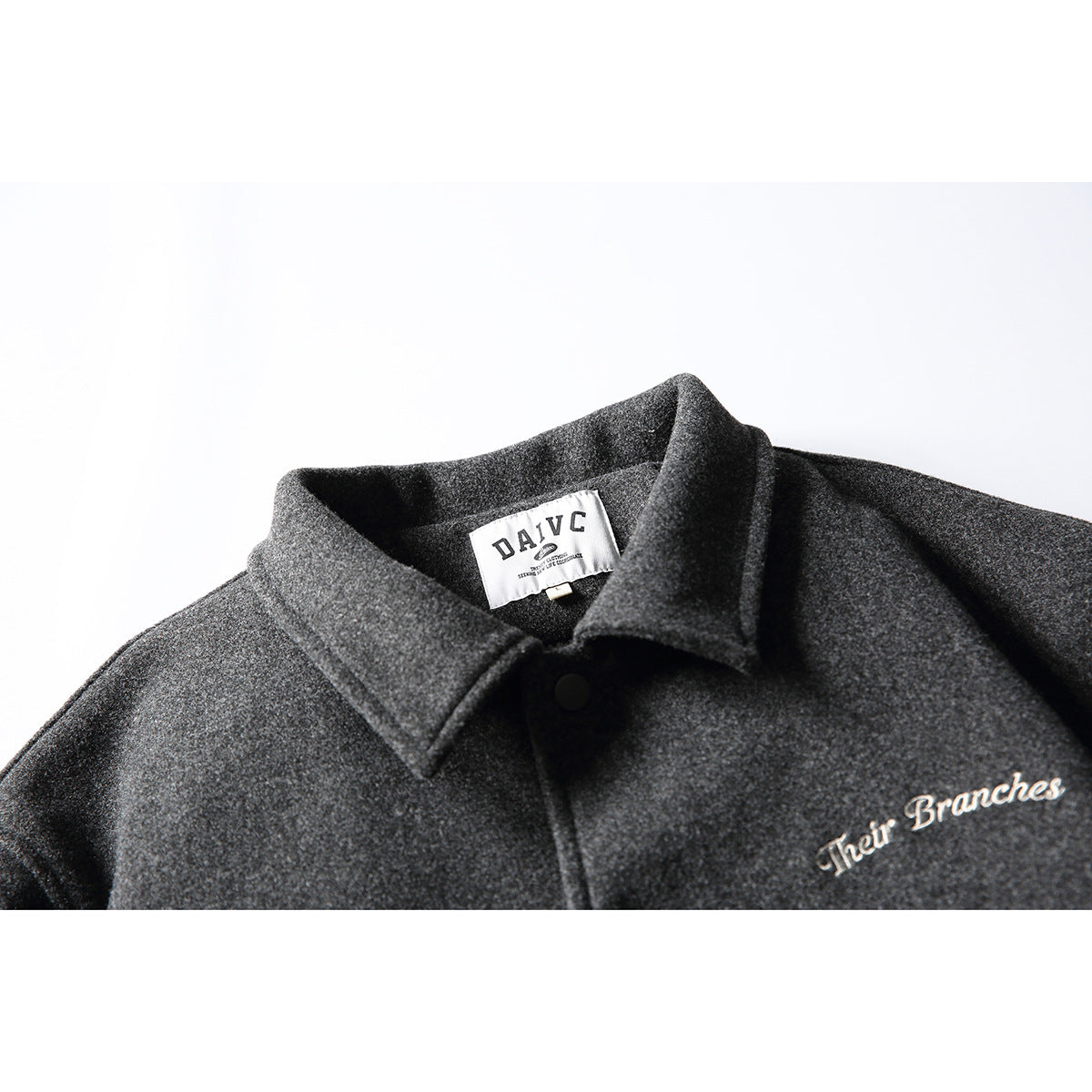 Close-up of a charcoal gray jacket collar, black snap, sewn neck label, and embroidered script on the chest.