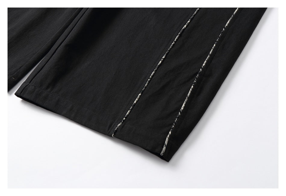 Close-up of black trouser leg hems with narrow plaid piping along the seams.