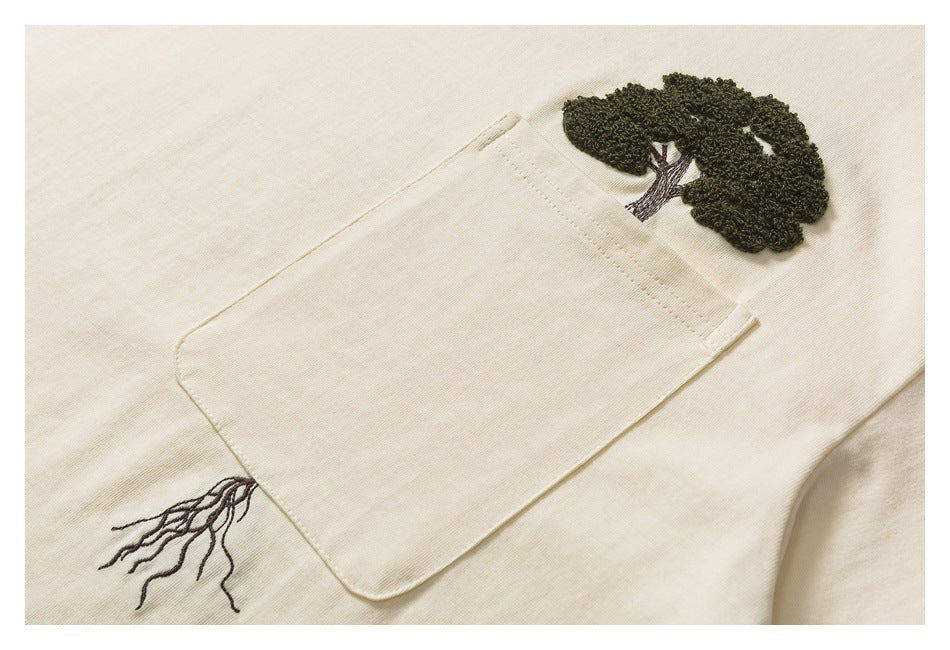 Close-up of a cream garment pocket with a dark embroidered tree motif and branching roots.