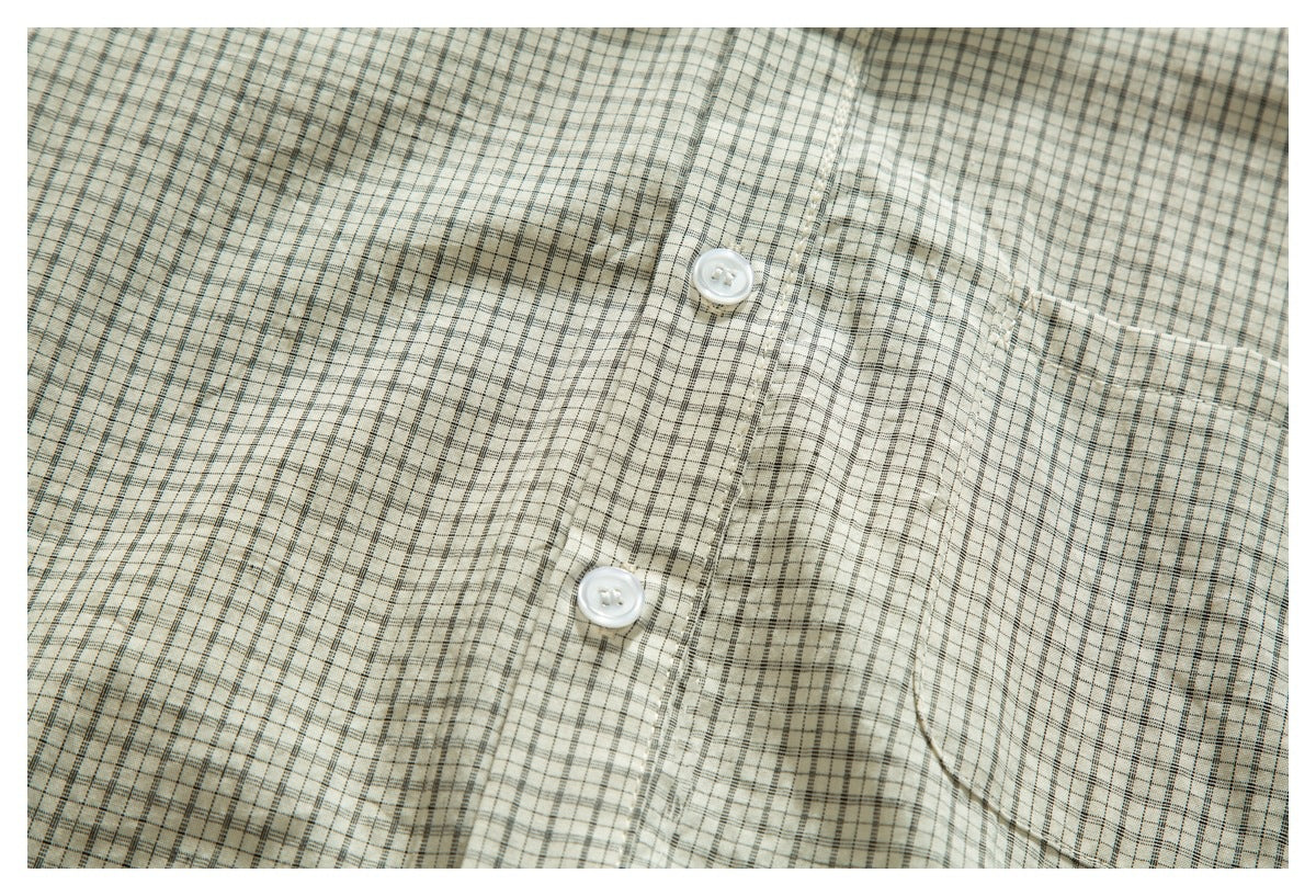 Close-up of the front of a cream plaid button-up shirt, showing white buttons and a chest pocket.