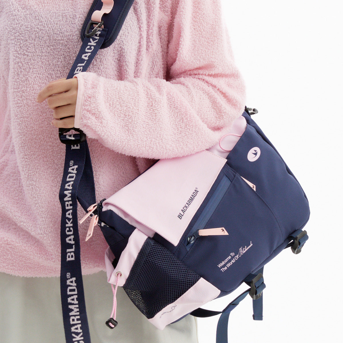 Close view of a navy and pale pink messenger bag worn over a pink fleece, showing its flap, straps, and pockets.