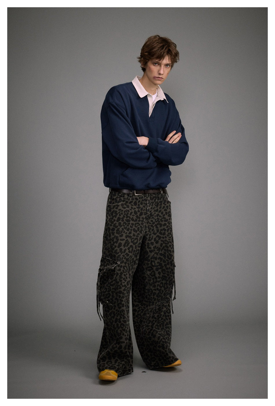 Model in a navy pullover and dark leopard-print cargo pants, standing at an angle with arms crossed.