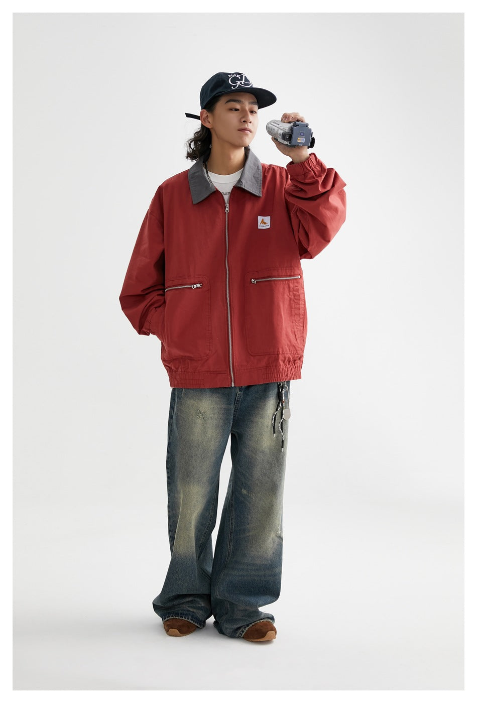 Full-length model wearing a rust-red jacket with gray collar and zip pockets, paired with wide-leg jeans.