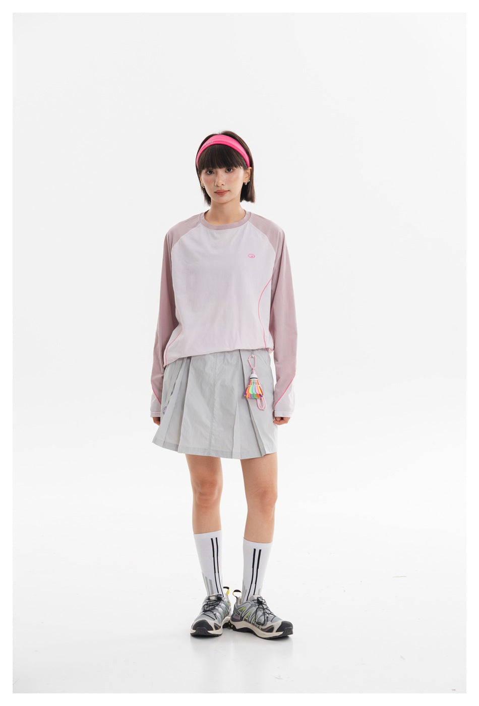 Full-length model view of a pale pink and white long-sleeve top with a light gray pleated mini skirt.