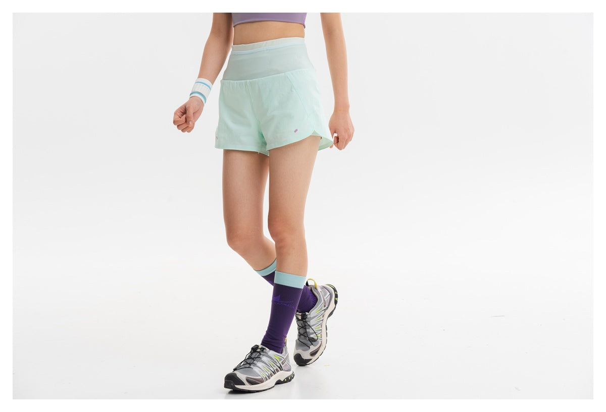 Cropped view of a model wearing mint athletic shorts, purple knee-high socks, and sneakers.