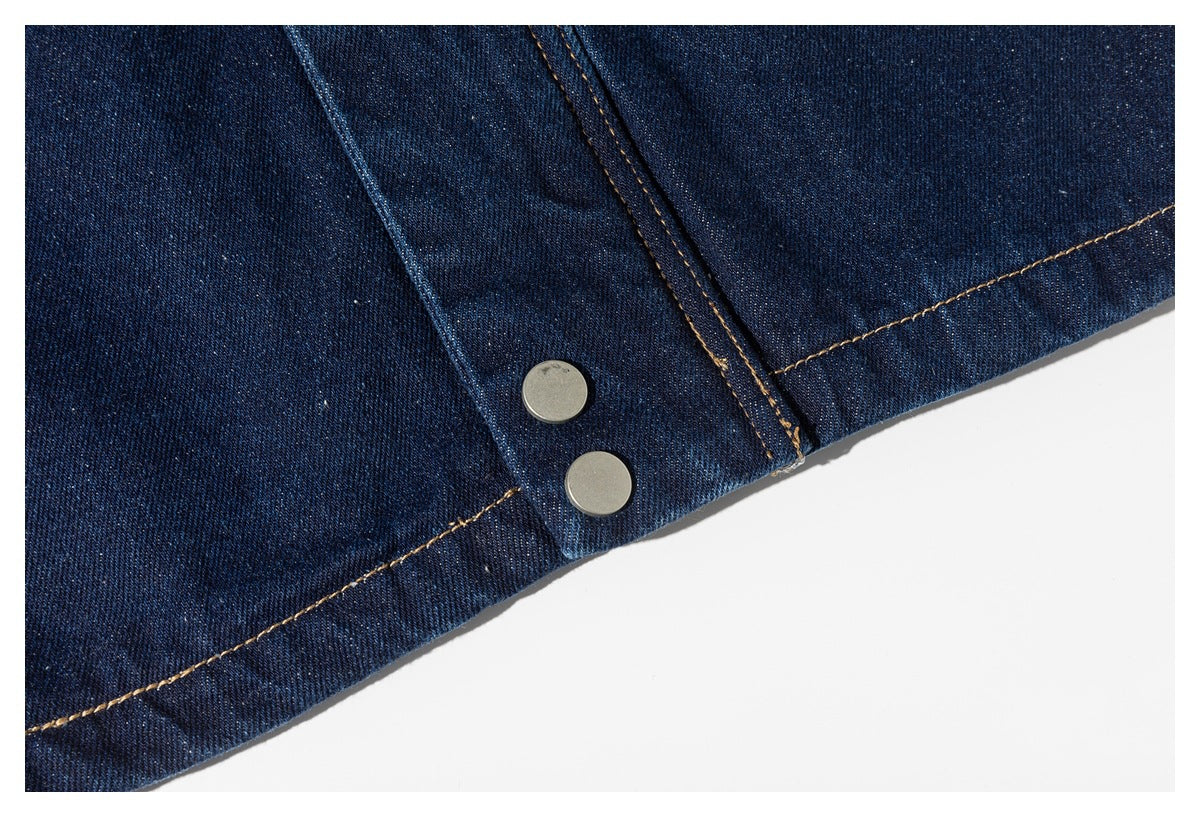 Close-up of two silver metal snap buttons and tan stitching on dark indigo denim.