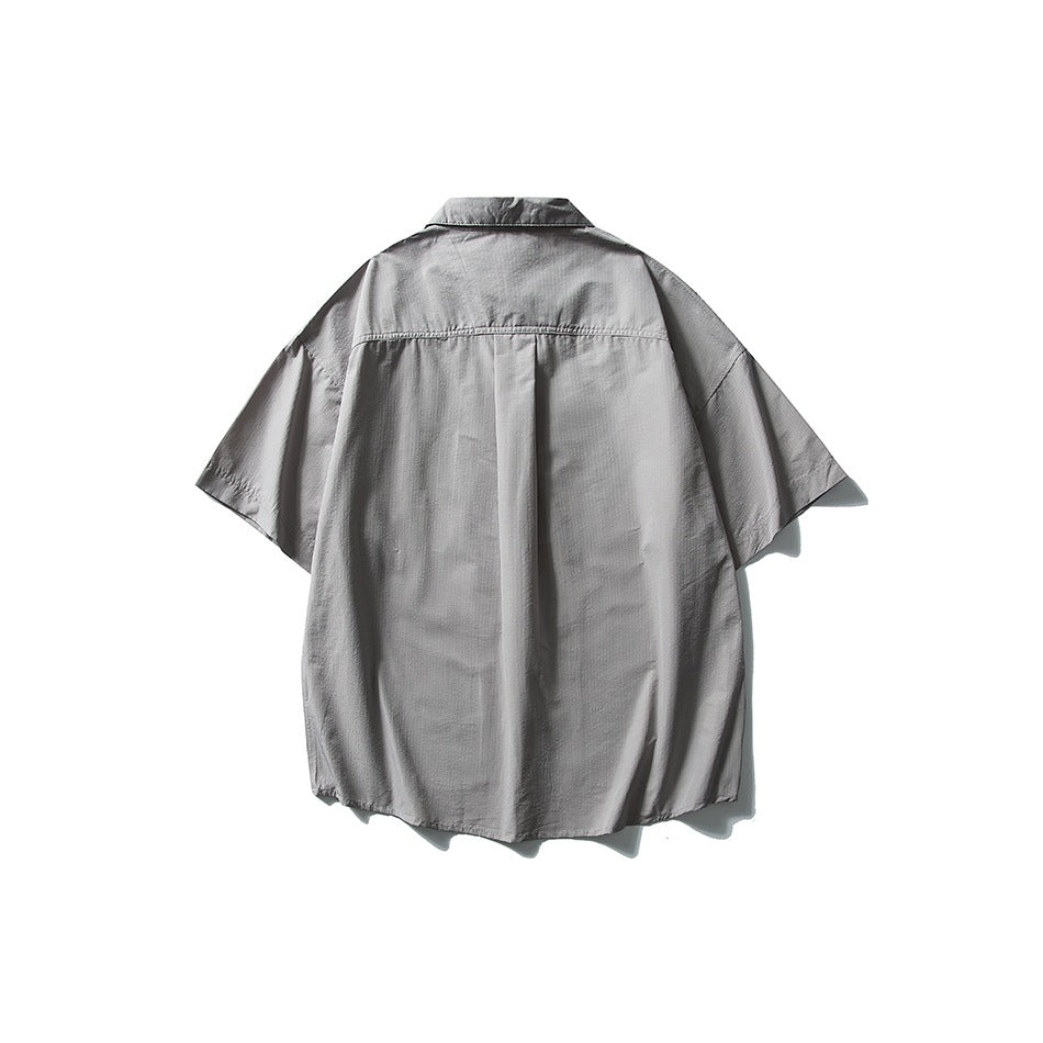 Back view of a gray short-sleeve collared shirt with a center pleat and curved hem, displayed against white.