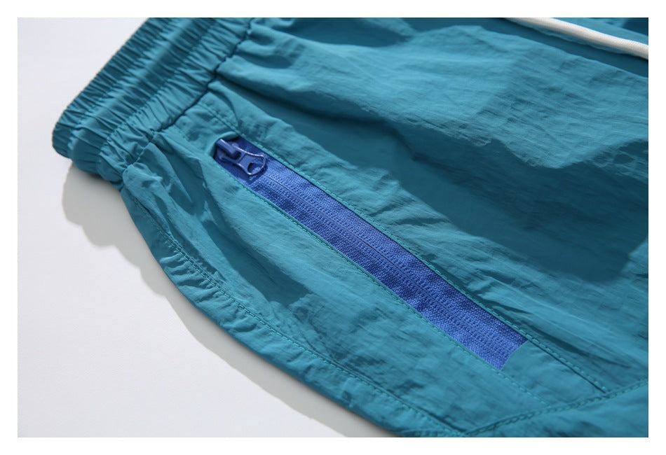 Close-up of teal shorts showing an elastic waistband and blue zippered pocket.