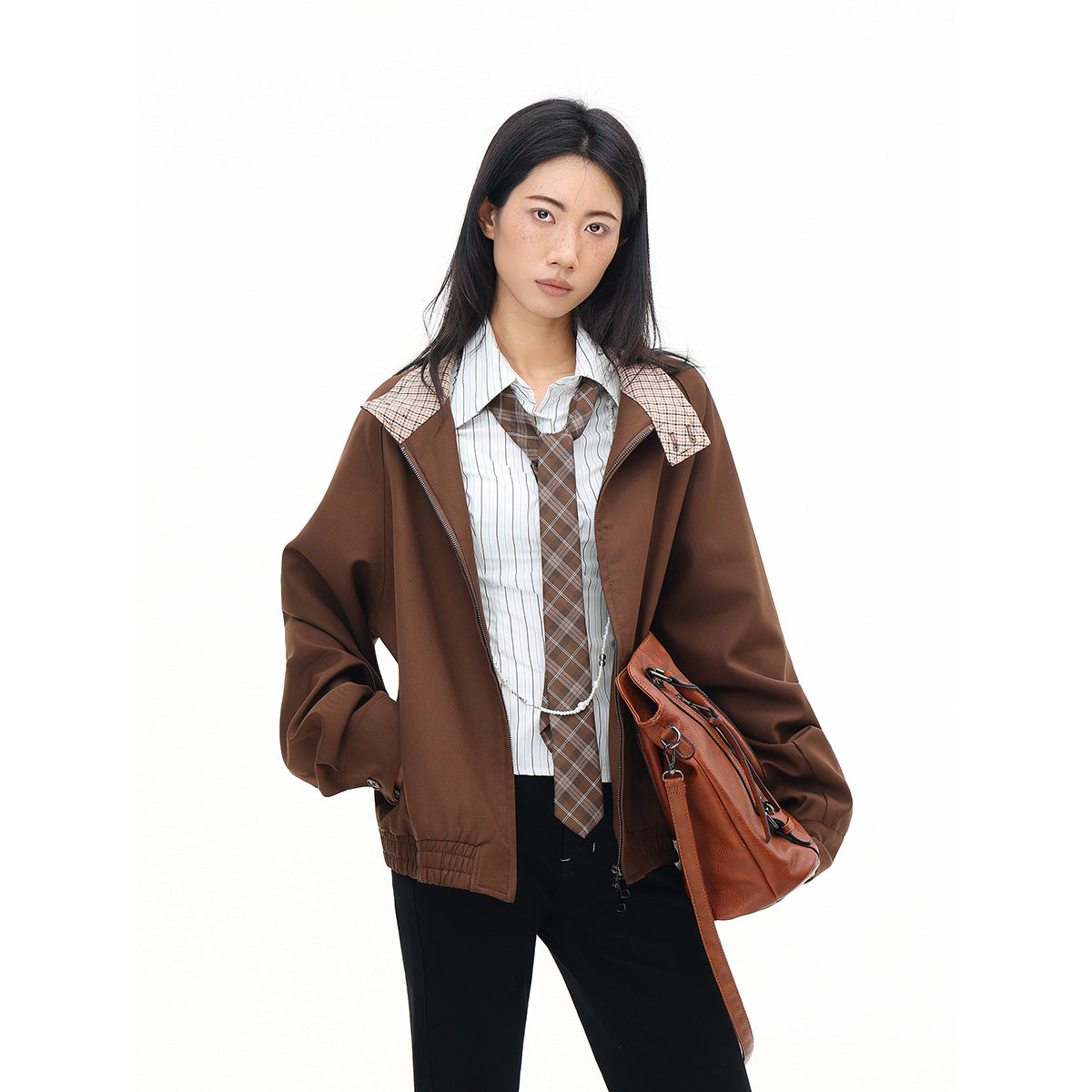 Model wearing an open brown jacket with plaid collar accents over a striped shirt and plaid tie; brown shoulder bag.