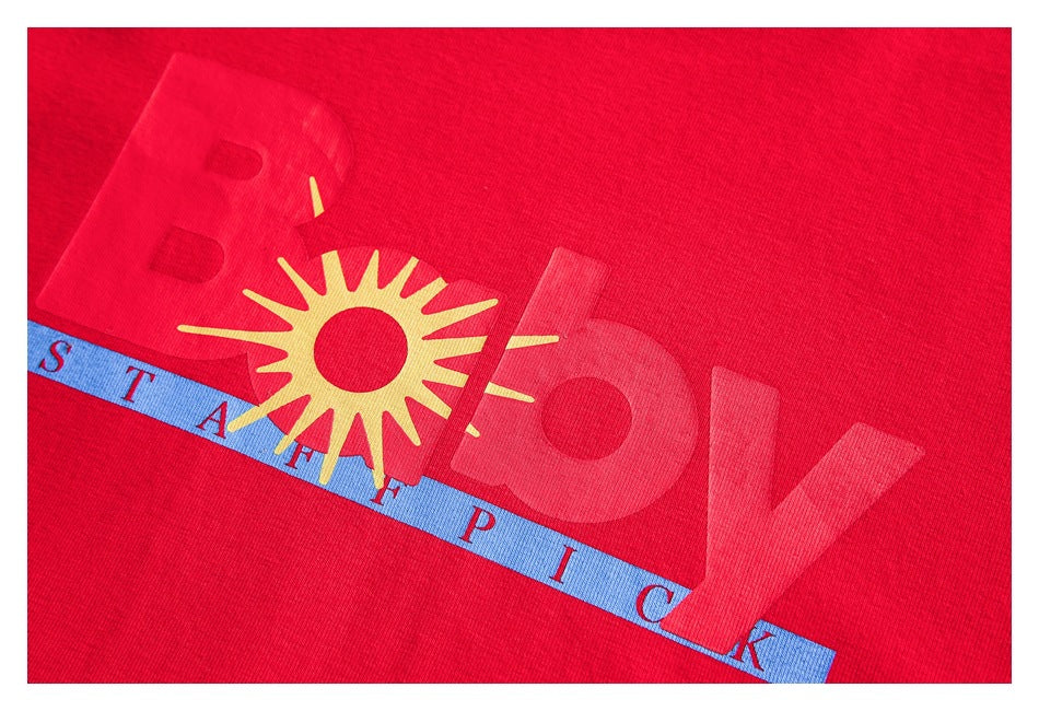 Close-up of a red garment graphic with a yellow sun, large tonal lettering, and a blue strip with English text.