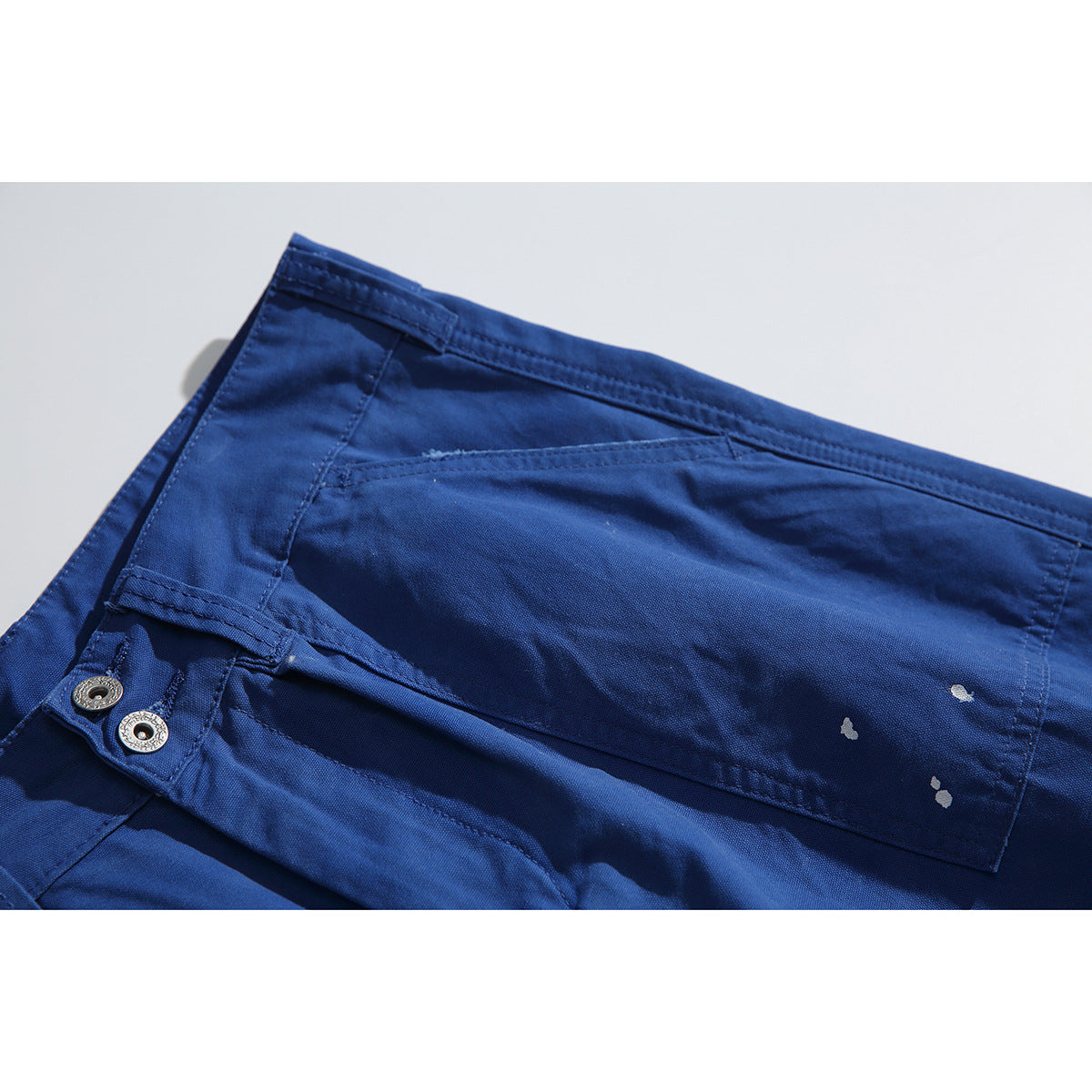 Close-up of cobalt-blue trousers showing a large patch pocket, waistband and white paint-like speckles.