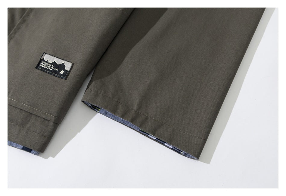 Close-up of a dark olive garment sleeve with a small sewn patch and checked fabric peeking from the hem.