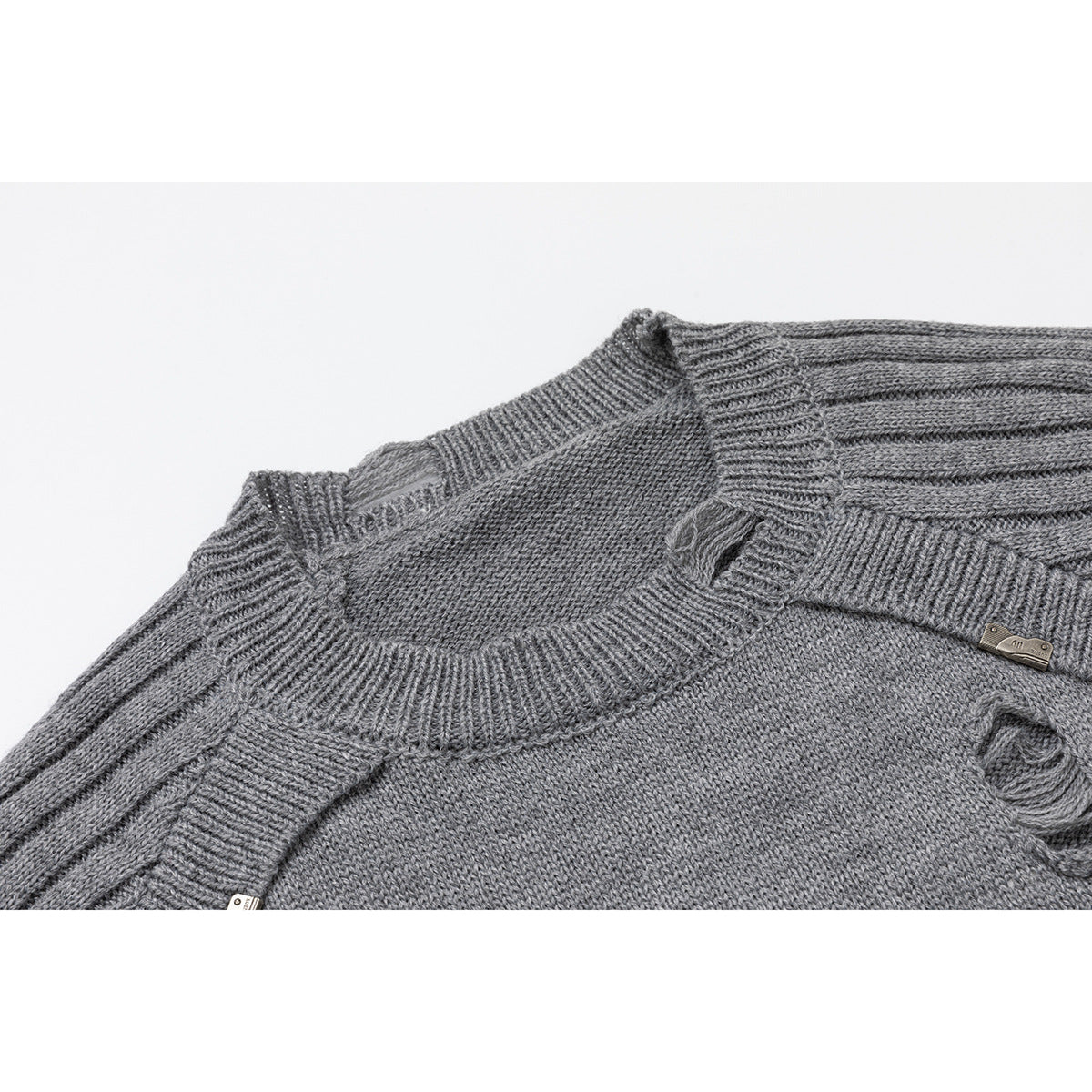 Close-up of a gray knit sweater showing its ribbed crew neck, shoulder seams, distressed holes, and small metal tag.