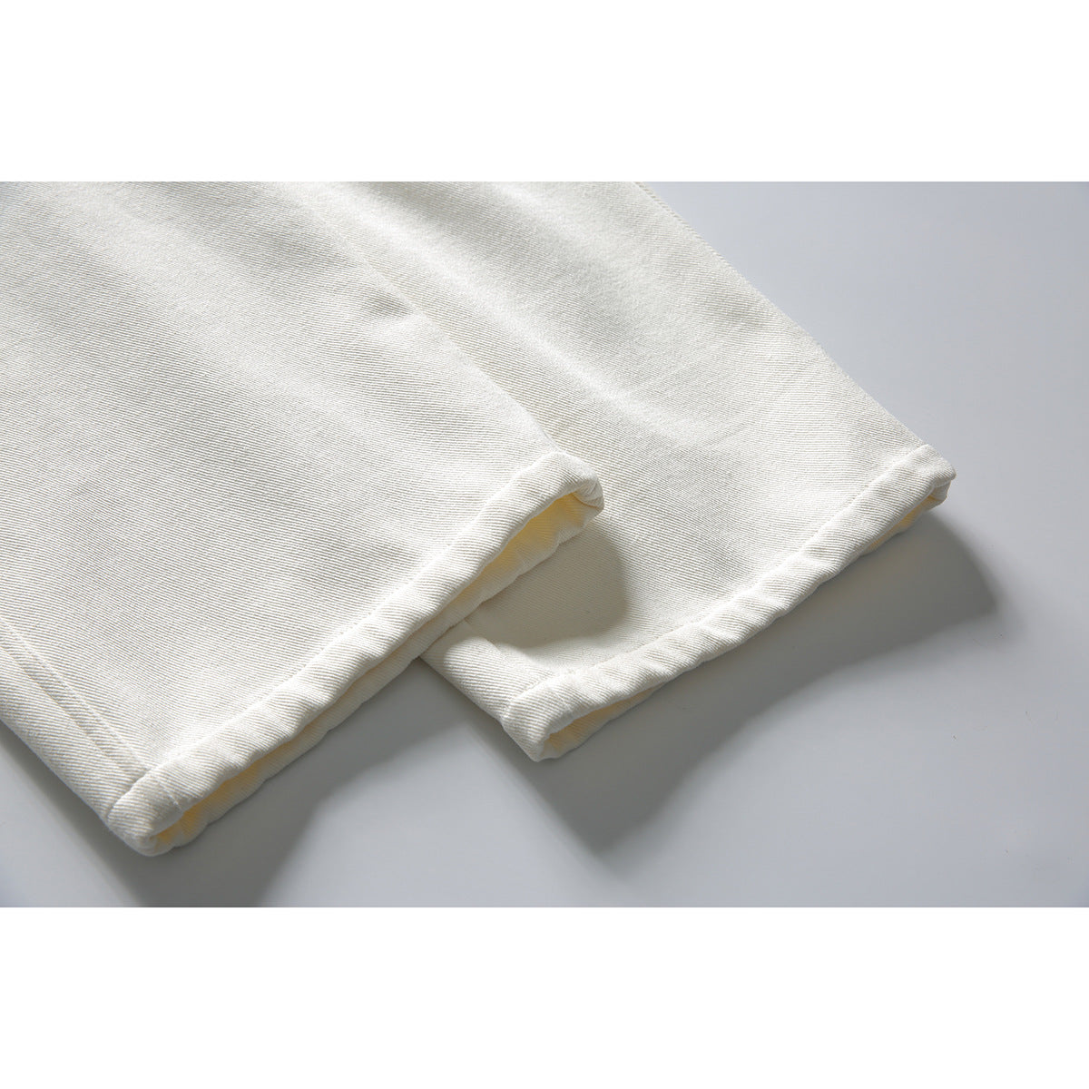 Close-up of off-white trouser legs showing the folded, stitched hems.