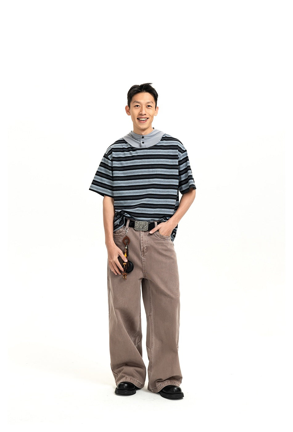 A man models a black and gray striped short-sleeve hooded shirt with loose taupe pants, facing forward.