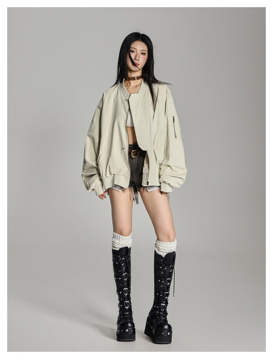 Model wearing an oversized beige bomber jacket open over a white top, denim shorts and black knee-high boots