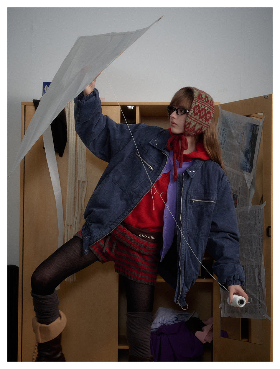 Model in a dark indigo zip jacket and patterned shorts, posing beneath an umbrella.