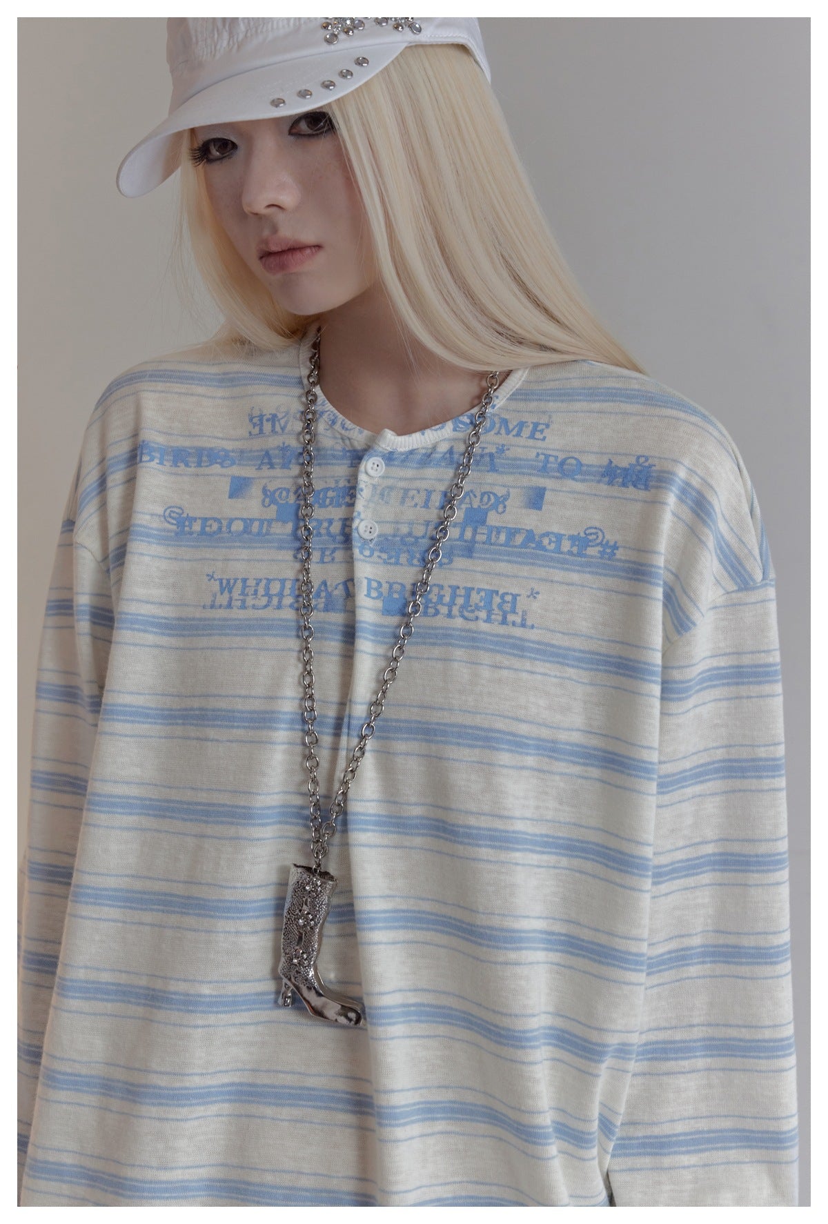 Model wearing a cream long-sleeve henley with thin blue stripes and distressed blue text print.