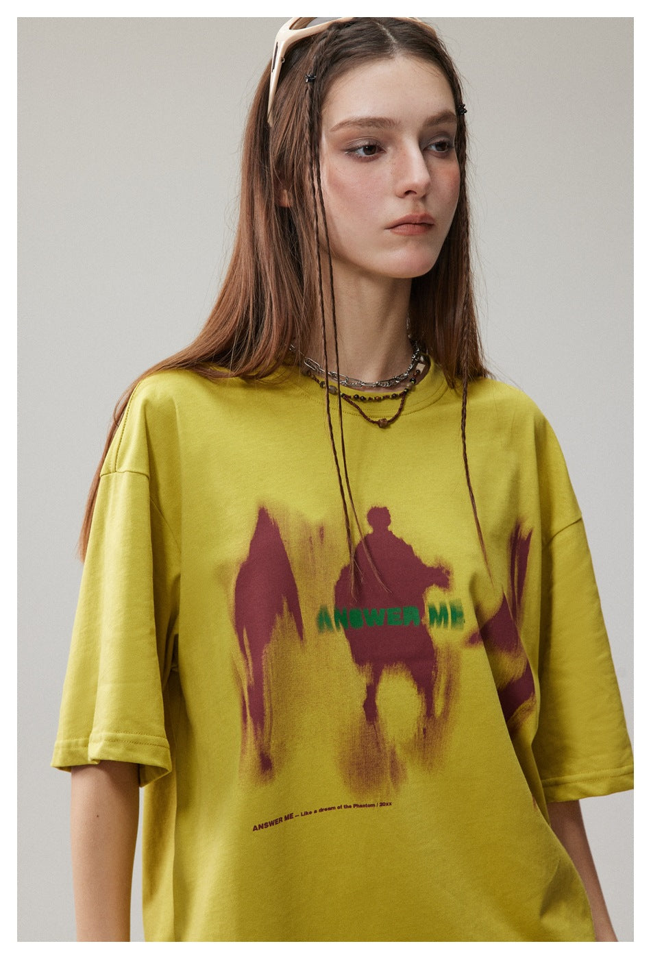 Close view of a model wearing a yellow T-shirt with burgundy abstract graphics and green lettering.