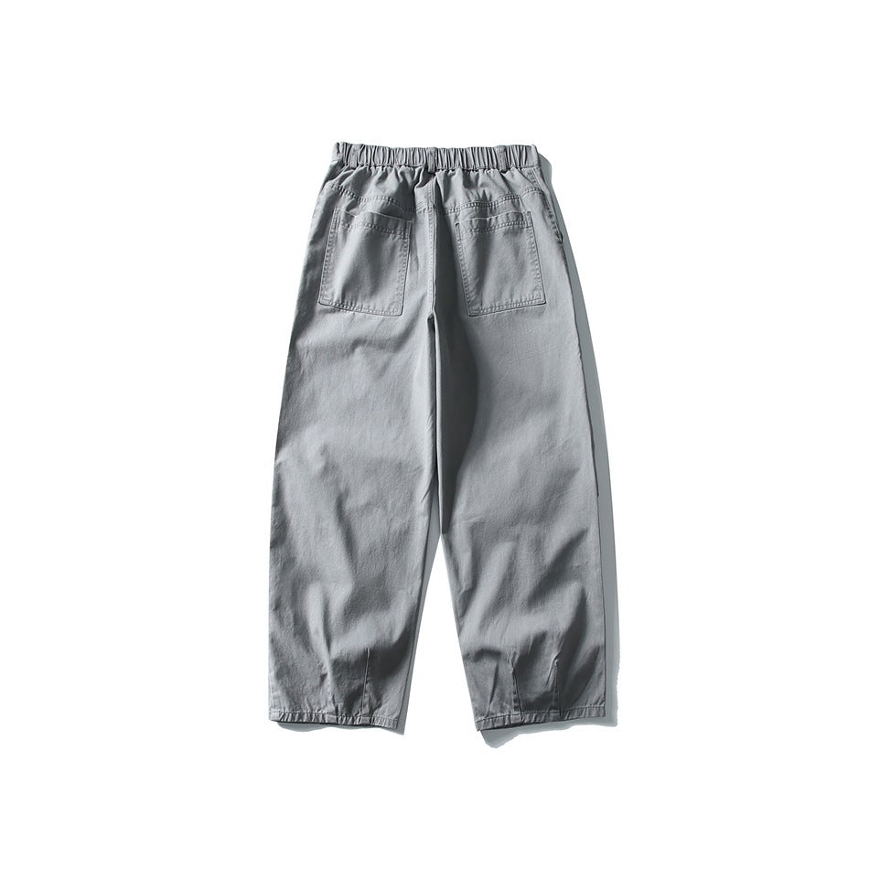 Back view of light gray loose trousers with an elastic waistband, two patch pockets and gathered ankle hems.