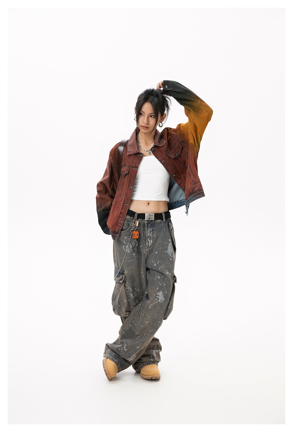 Model wearing a rust-red denim jacket with mustard and black gradient sleeves, white crop top, and charcoal cargo jeans.