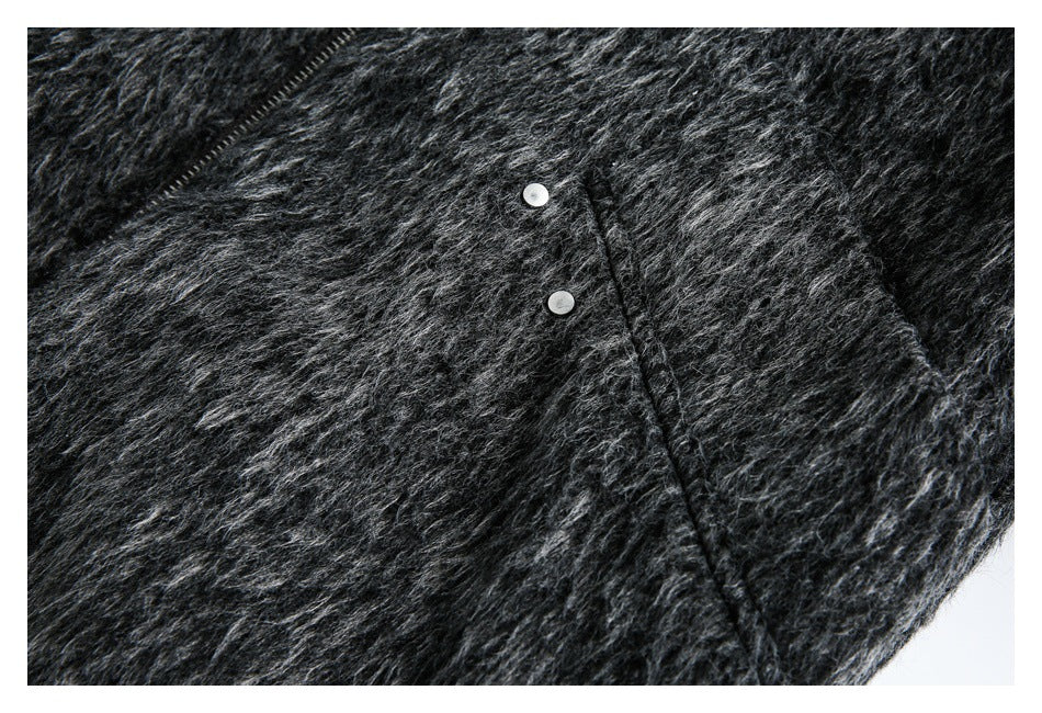 Close-up of a charcoal-black fuzzy garment with two silver snaps and a diagonal zipper edge.