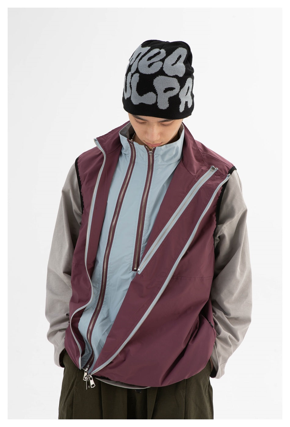 Model shows a plum vest worn open over a pale blue-gray zip-front jacket, revealing layered zippers.