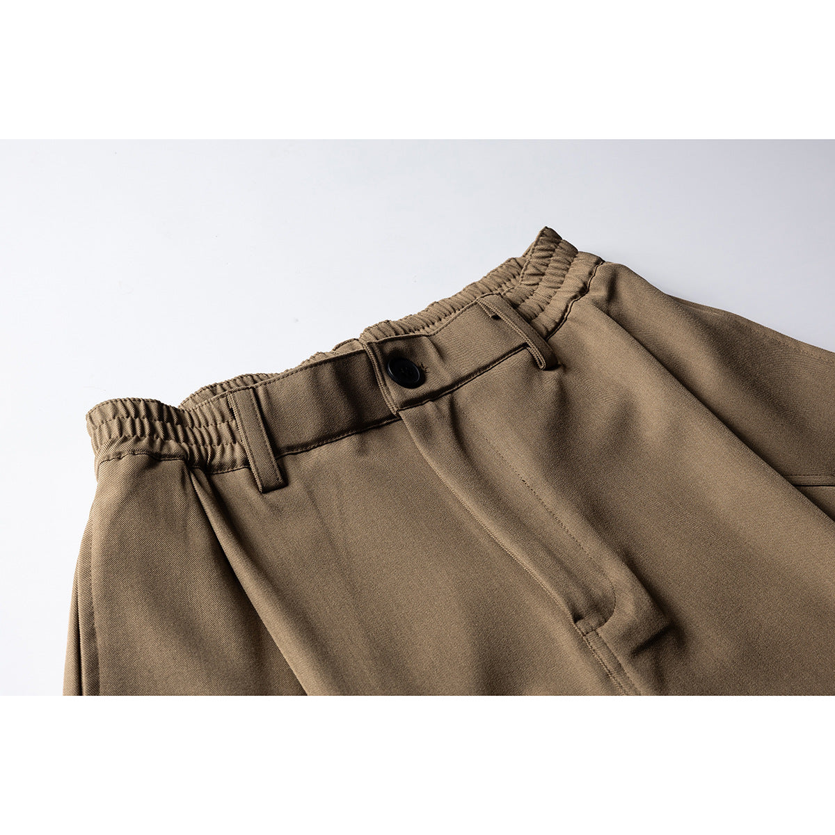 Close-up of brown shorts showing the elasticated waistband, belt loops, black button and front fly.