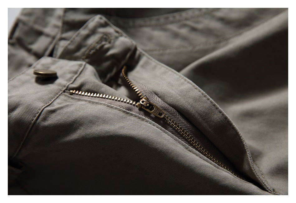 Close-up of the metal zipper and waistband button on taupe-gray trousers.