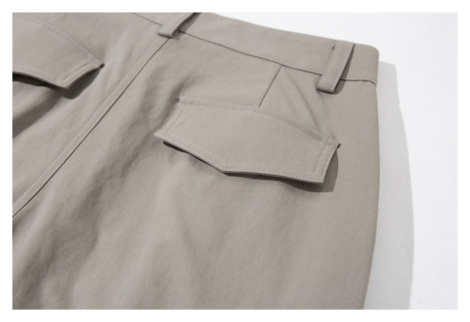 Close-up of taupe-gray trousers showing the waistband, belt loops, and a small flap pocket.