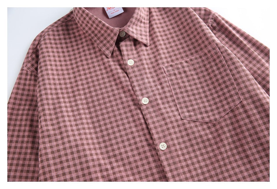 Close view of a dusty pink and brown checked button-up shirt front, showing its collar, placket and chest pocket.