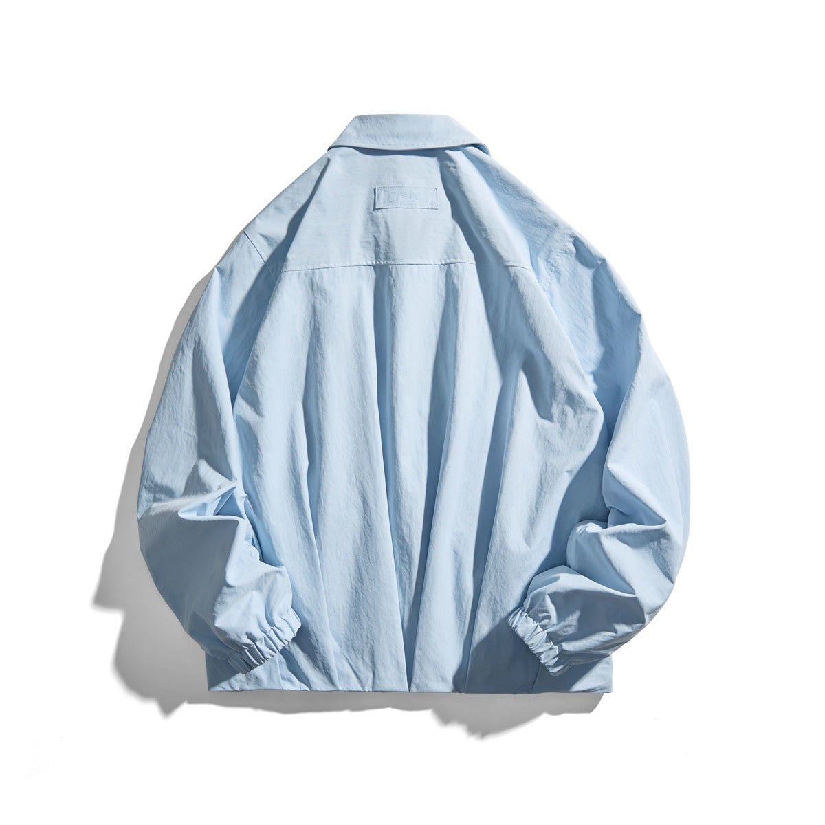 Back view of a light blue collared jacket with a shoulder yoke, center seam, and elastic cuffs.