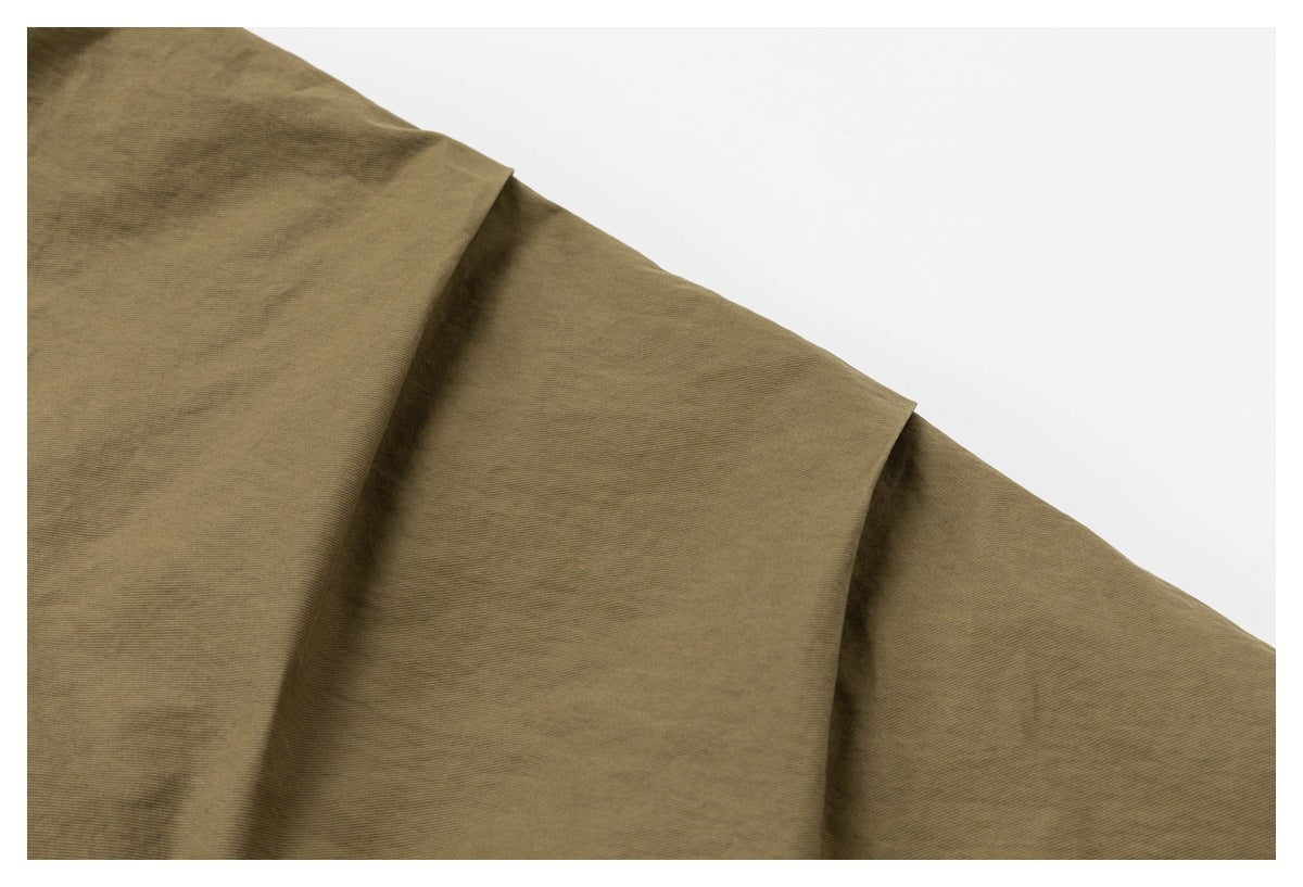 Close-up of khaki-brown fabric draped in broad folds against a white background.