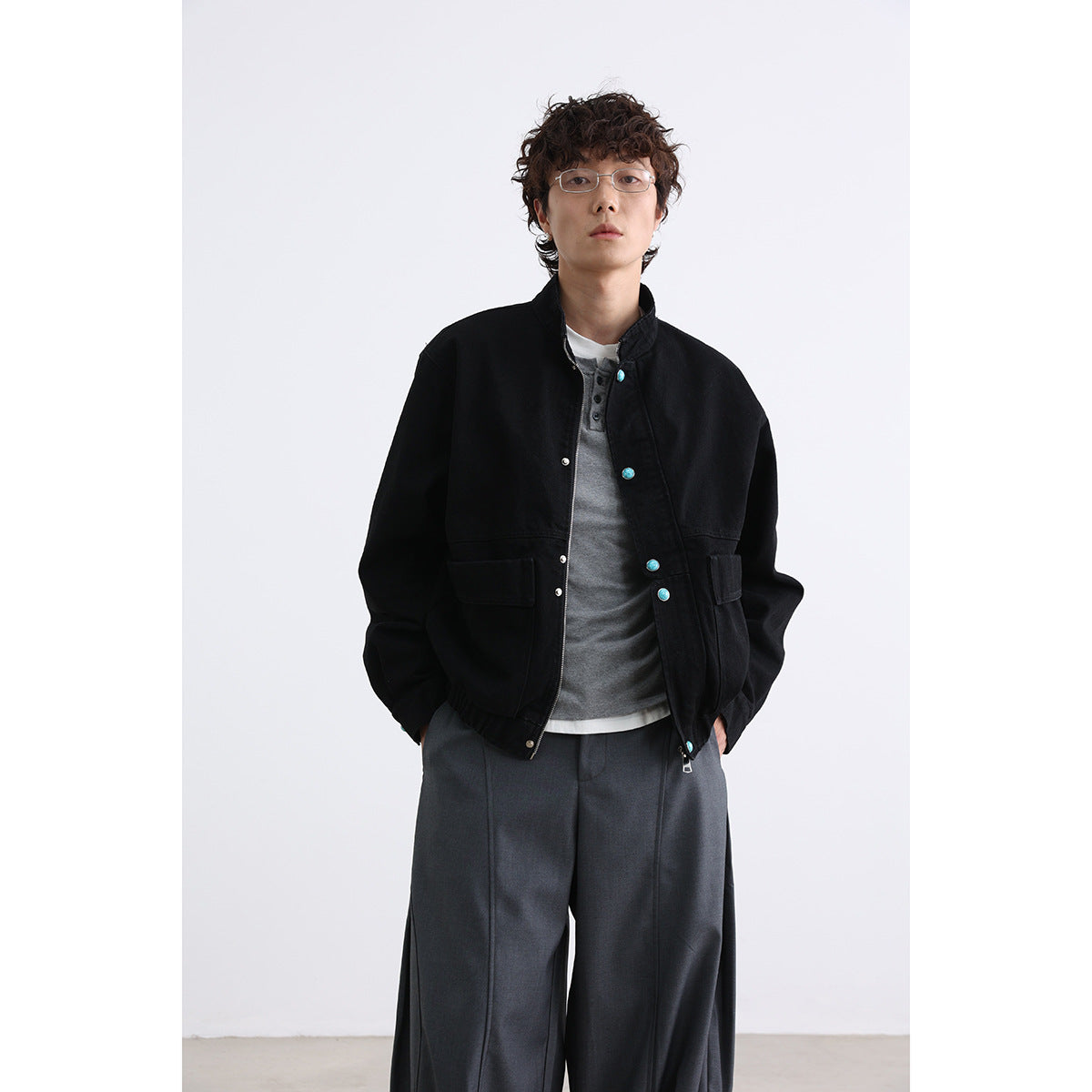 Model wearing a black stand-collar jacket with turquoise buttons and wide charcoal trousers, front view.