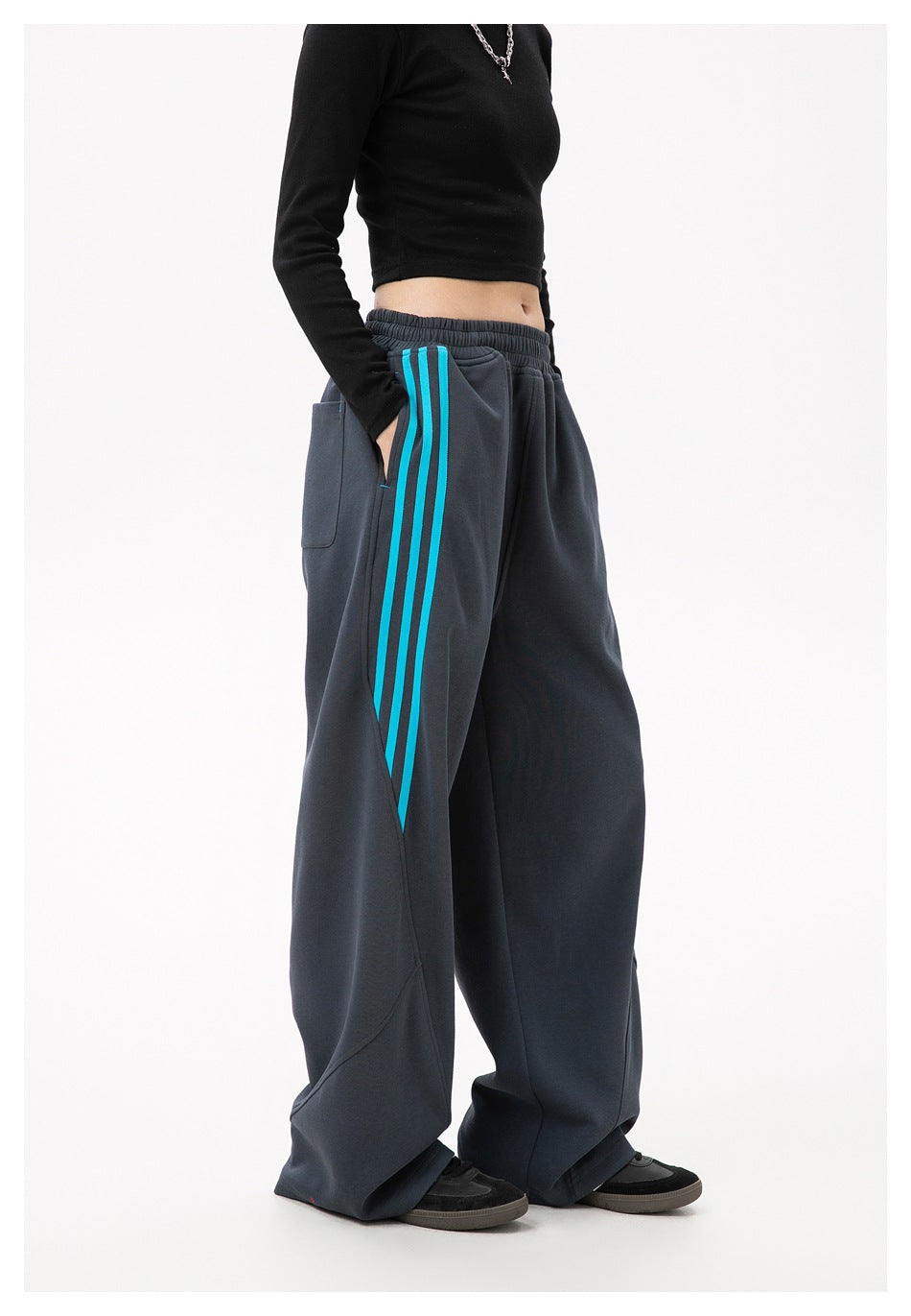 Side view of charcoal wide-leg pants showing turquoise stripes and a rear patch pocket, worn by a model.
