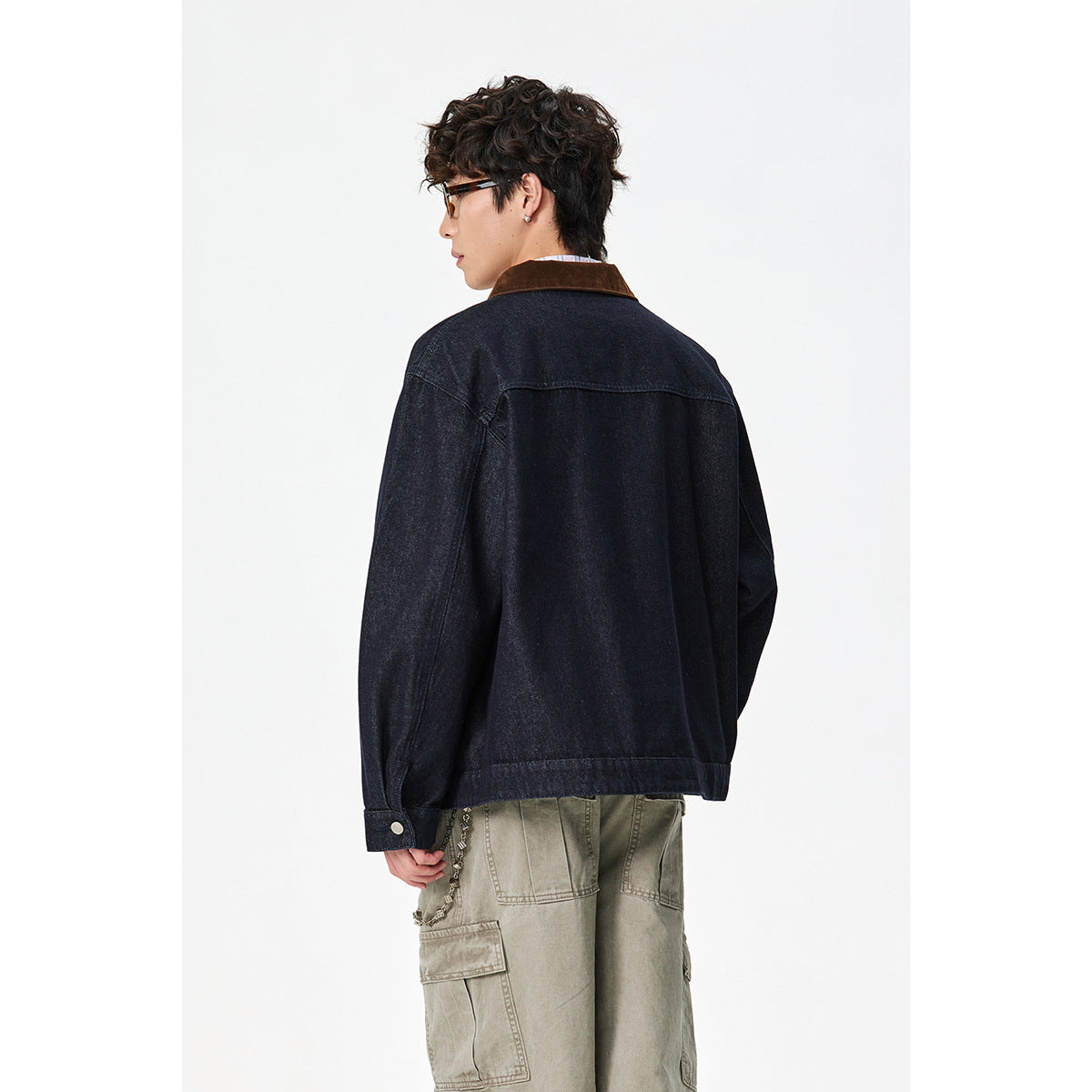 Rear view of a model wearing a dark indigo jacket with a brown collar and khaki cargo pants.