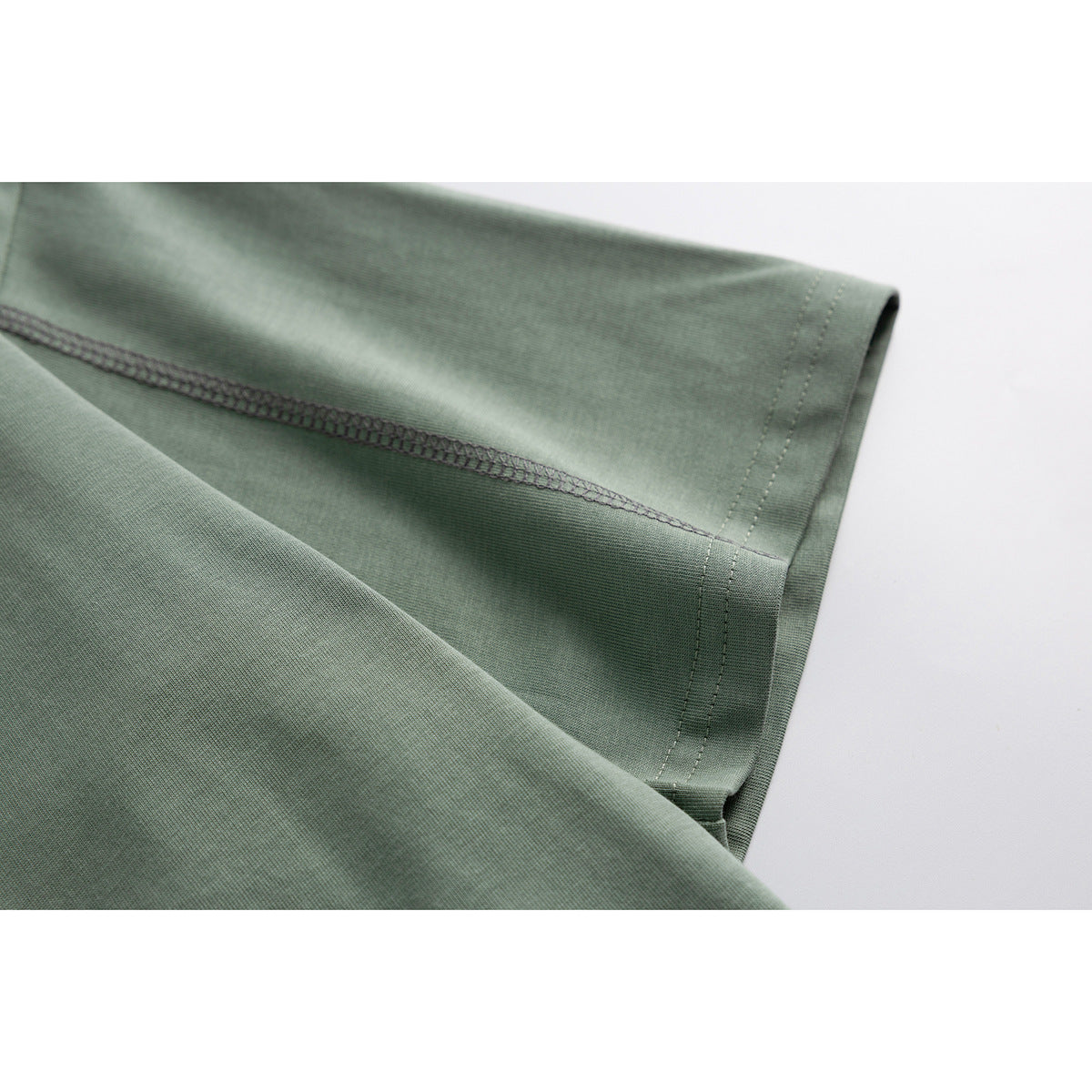 Close-up of the sage green T-shirt's short sleeve hem and dark overlock stitching.