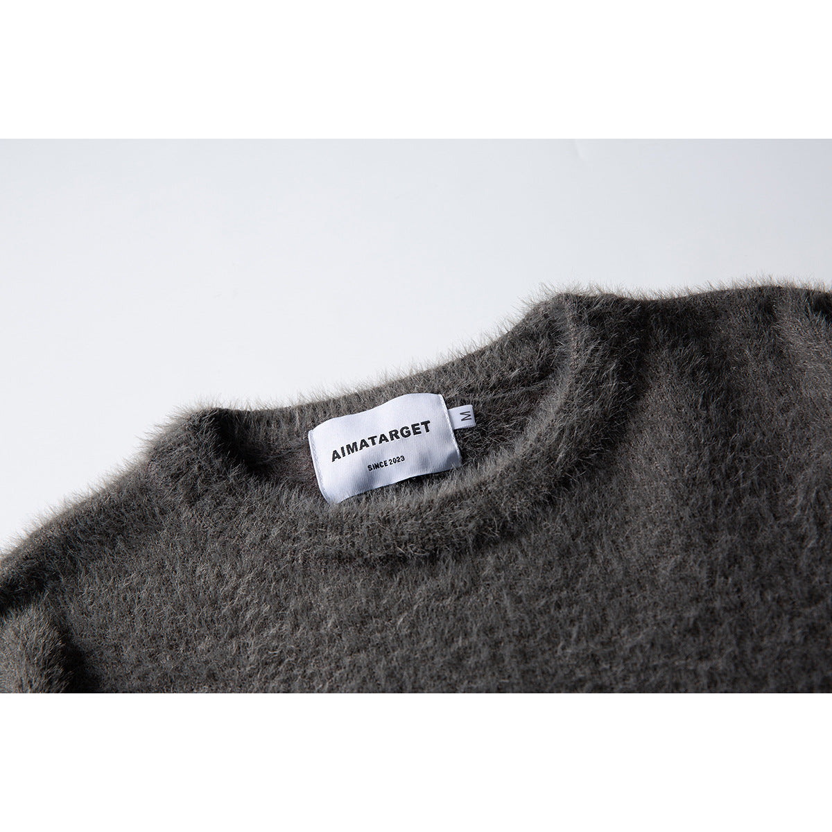 Close-up of a fuzzy charcoal-gray sweater neckline with a sewn white AIMATARGET label.
