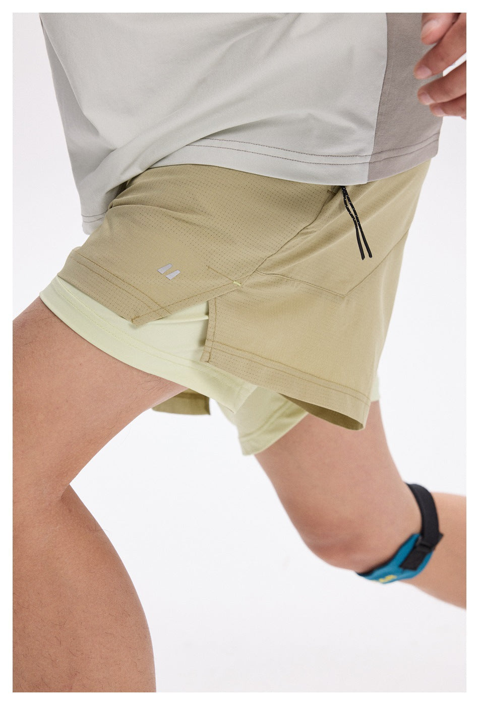 Close-up of khaki layered running shorts showing the side zip pocket, small logo, and pale inner shorts.