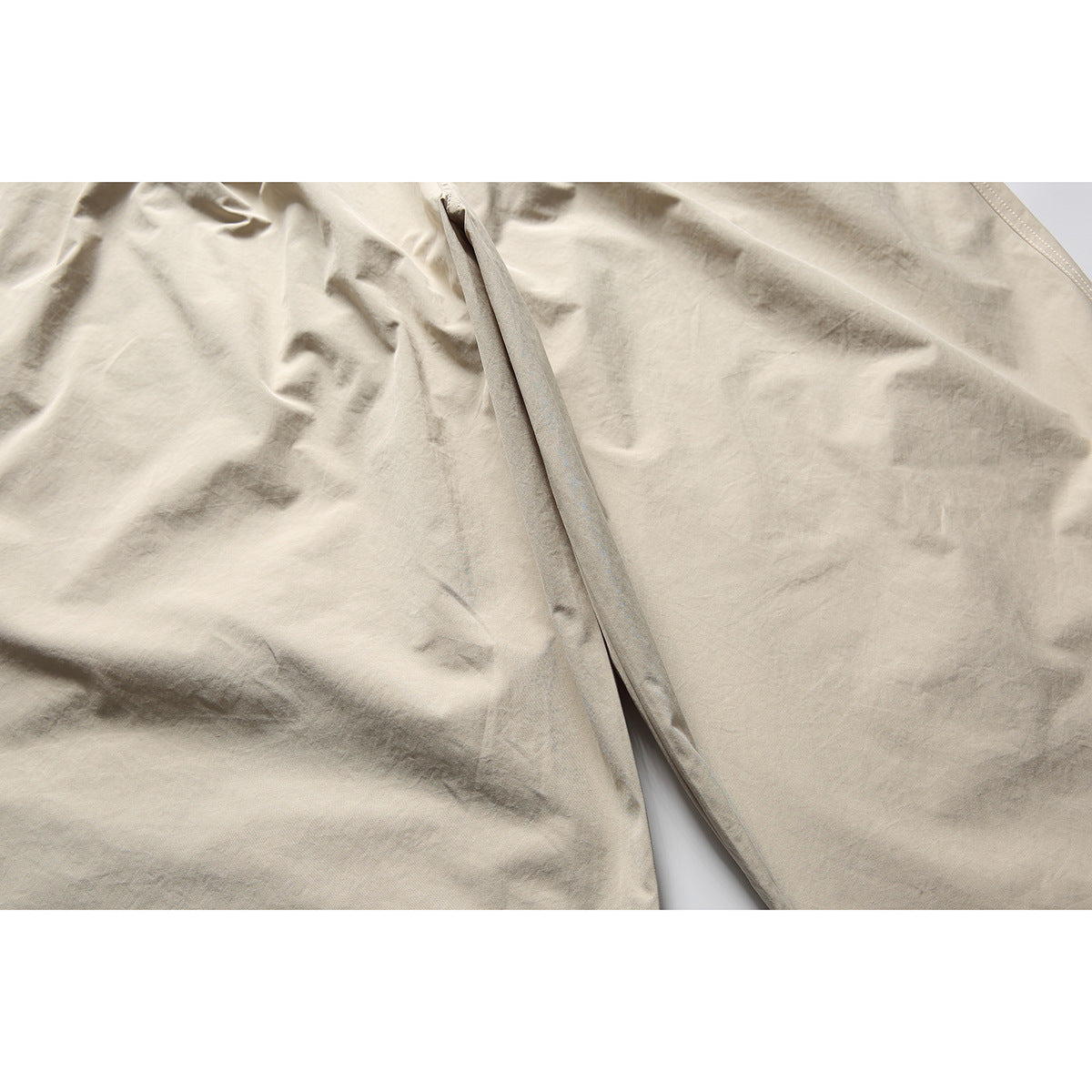 Close-up of light beige pants showing the central seam and overlapping fabric panels.
