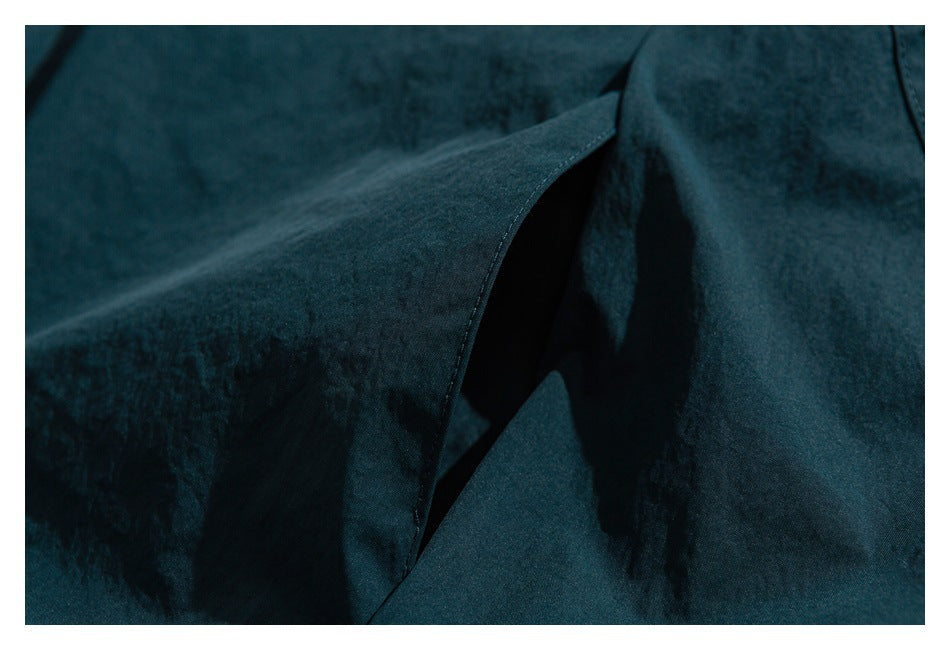Close-up of dark teal garment fabric and a curved overlapping flap or opening.