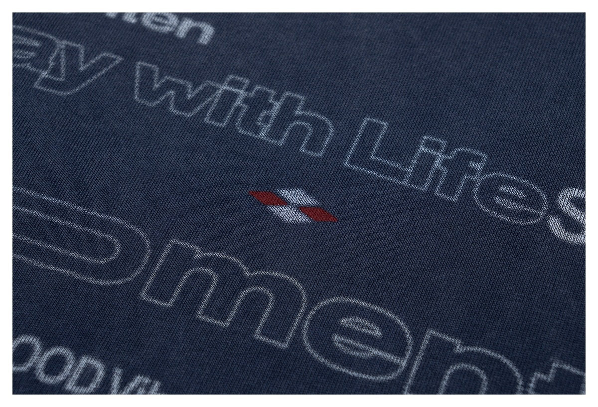 Close-up of the T-shirt's light-colored English lettering and small red-and-white graphic print.