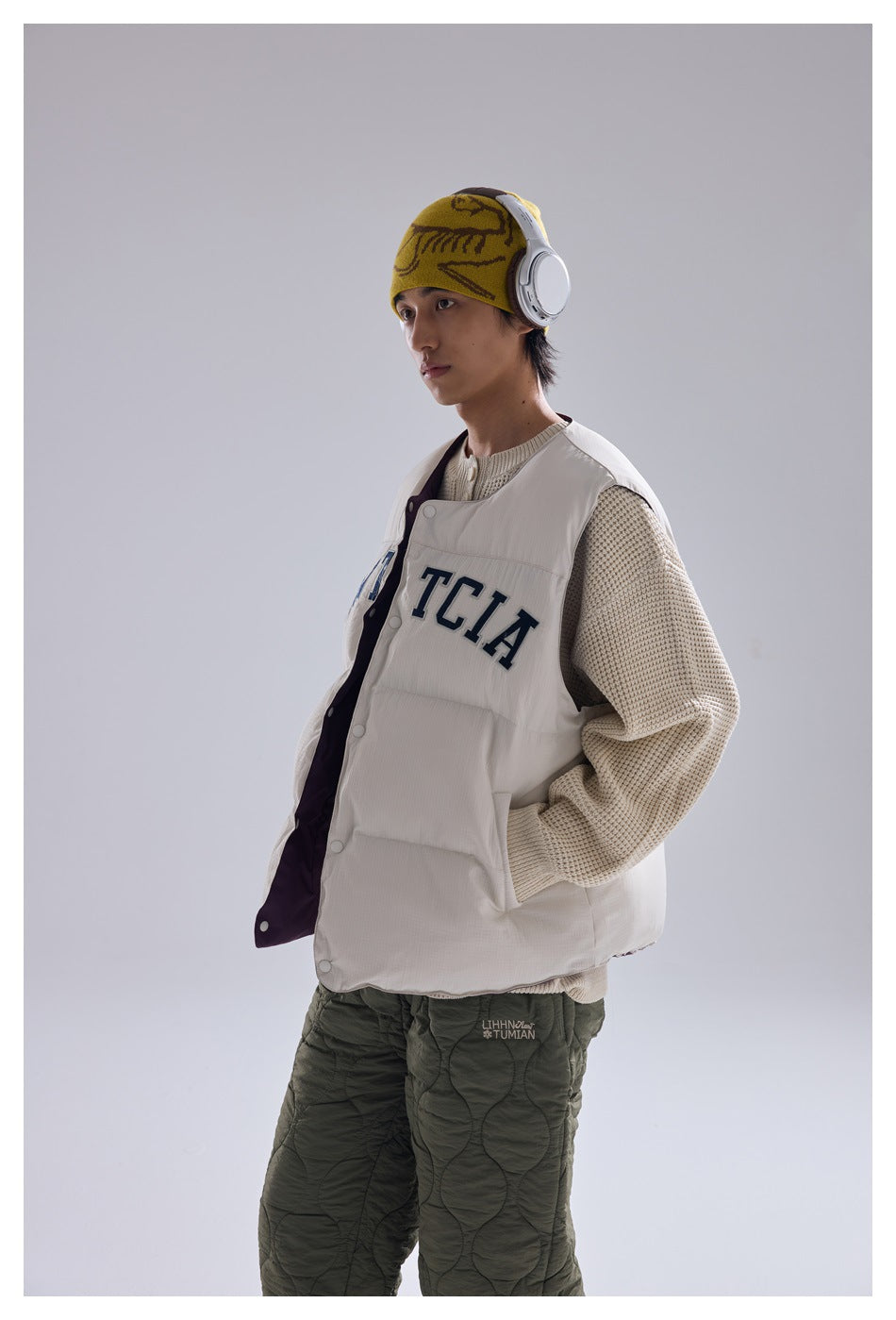 Side view of person wearing off-white puffer vest with snap front over a beige knit sweater, hand in pocket